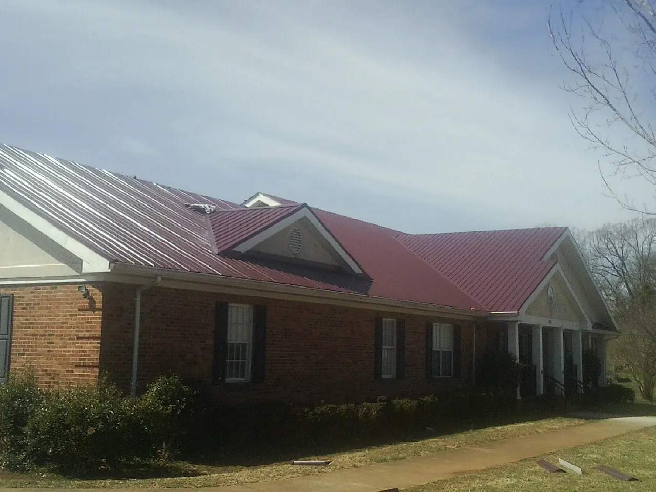 Red metal roof with gabled entries on a long brick building, from a Hail Damage Roof Repair job in Baldwin Place