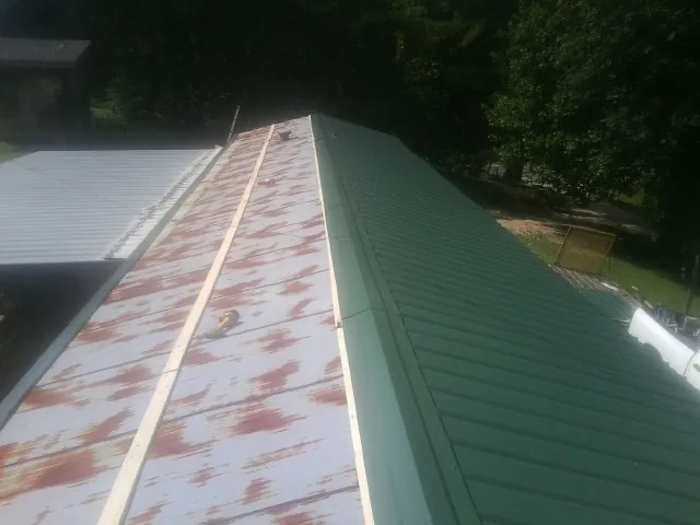 Old rusted panels beside newly installed green metal roofing — Wind Damage Roof Repair by Roofing Brothers in Baldwin Place