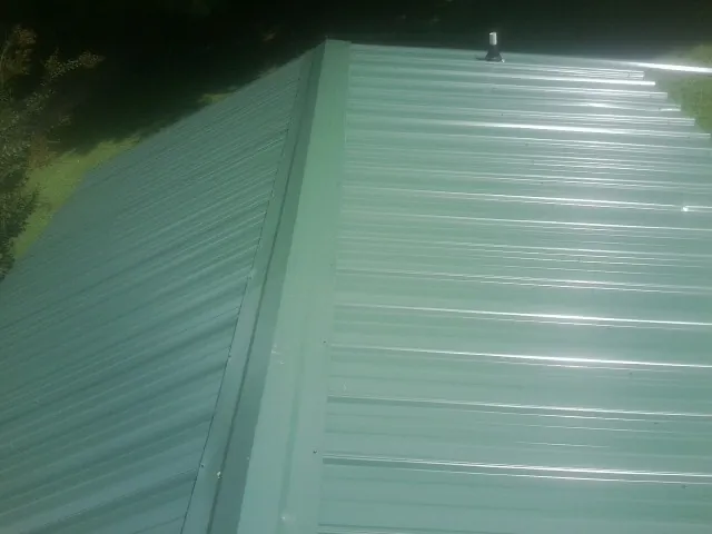 New green metal panels meeting at the ridge of a roof — Flat Roof Repair work by our crew in Baldwin Place