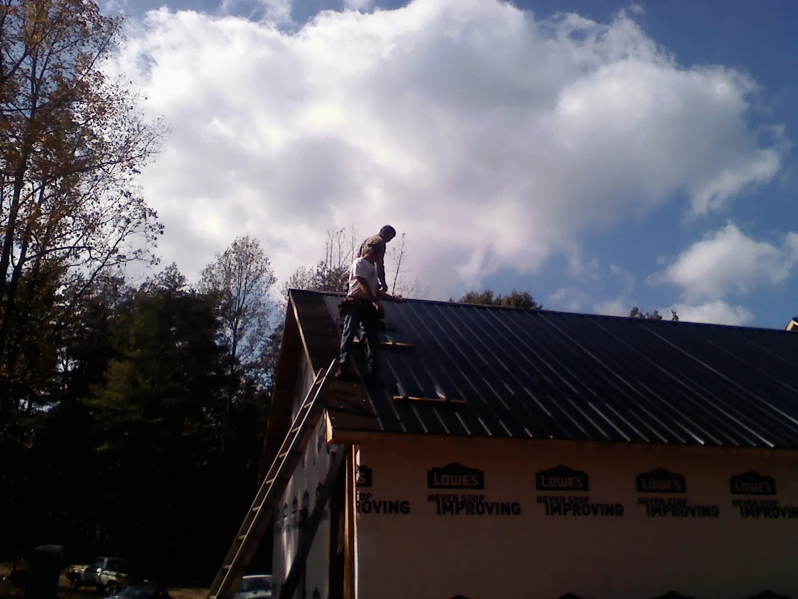 Roofer fastening dark metal panels high against a cloudy sky, from a Roof Inspection job in Baldwin Place