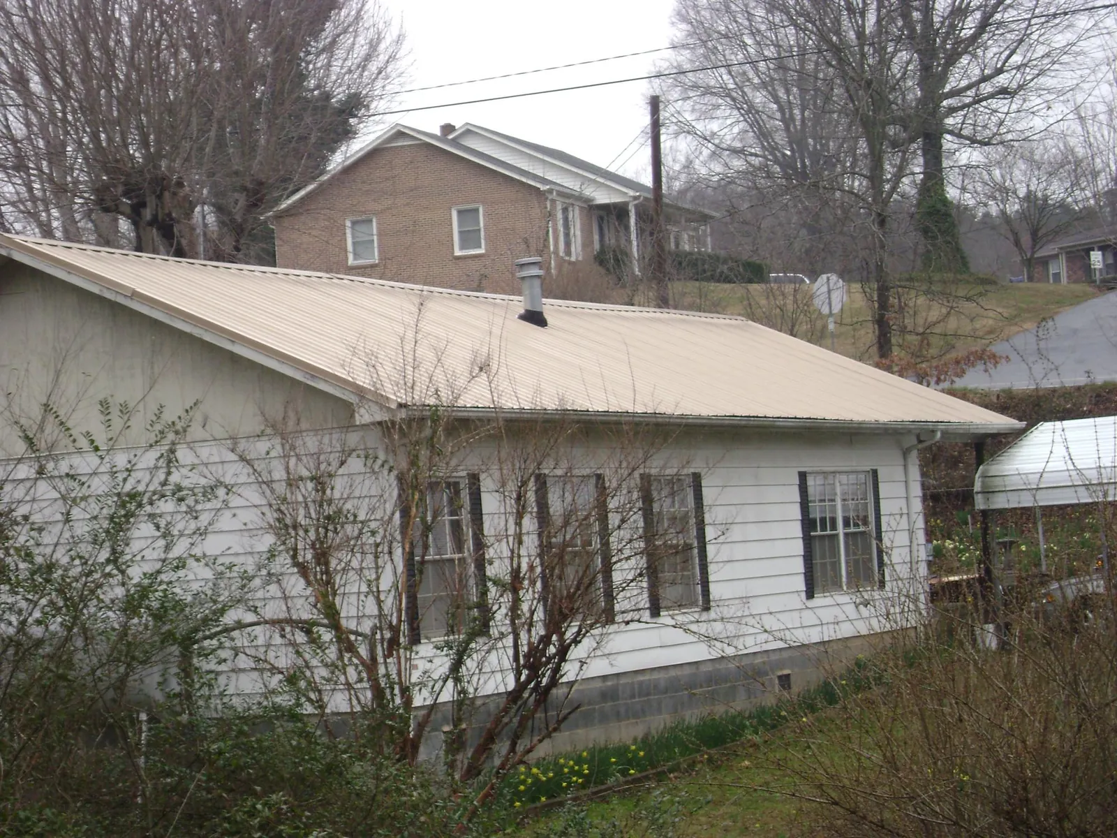 Tan metal roof on a white sided house set into a hillside — Commercial Roofing by Roofing Brothers in Baldwin Place